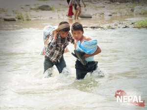 Two Nepali boys help each other cross the river, carrying 66 lbs. rice and a tent after a recent relief distribution event. (Photo, caption courtesy GFA)