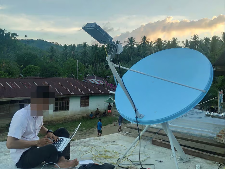 Man sits next to satellite.