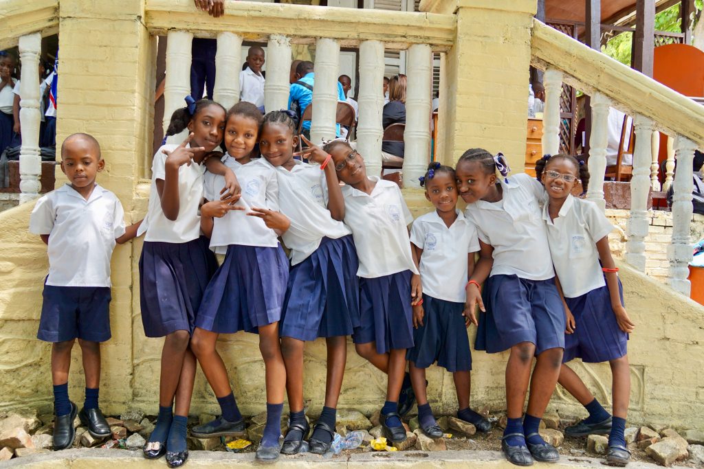 A line of children in uniforms stand and smile at camera.